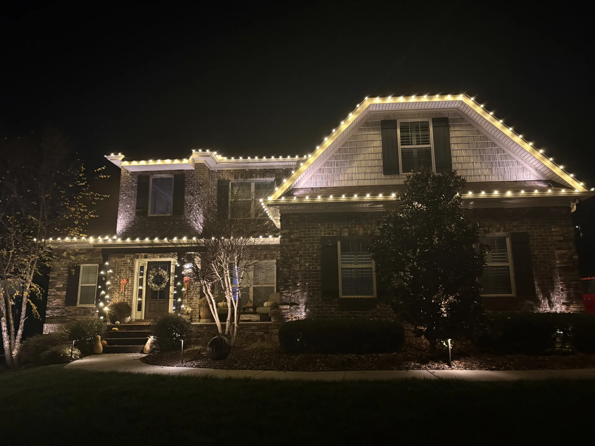 Holiday lights along multiple roof levels and the entrance of a brick home